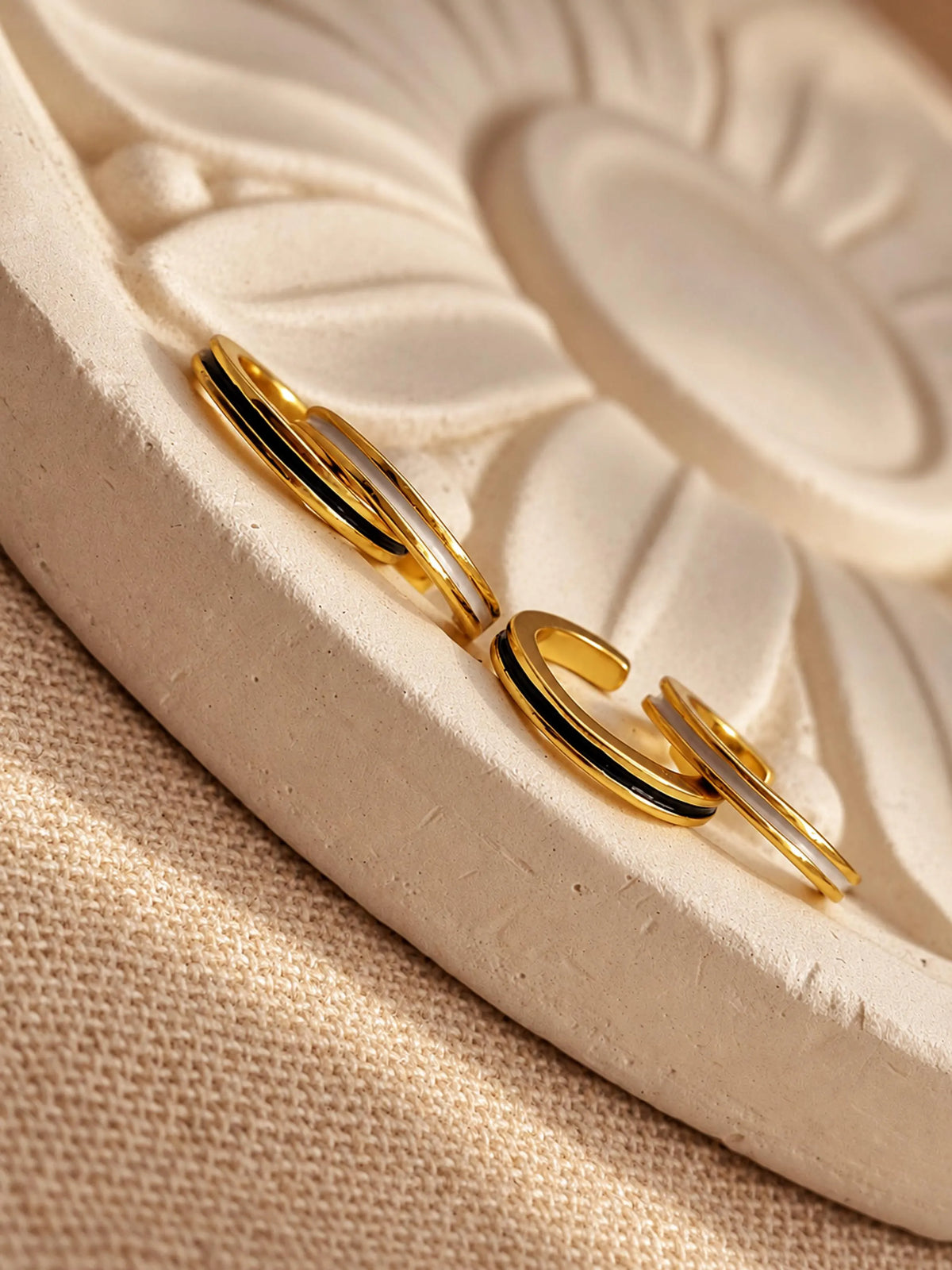 Black and white enamel ear cuffs displayed on a neutral ceramic dish showing the curved open design.