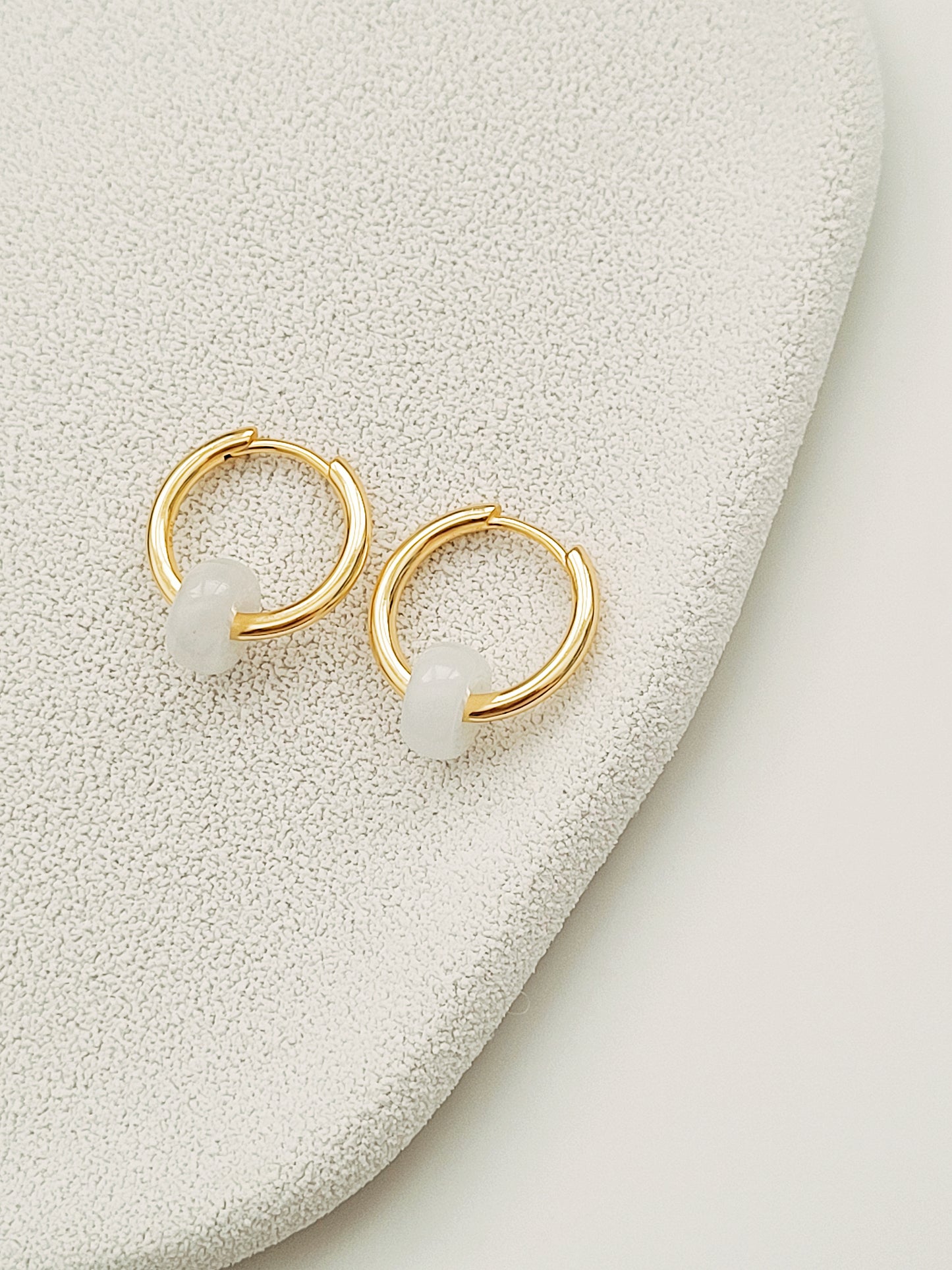 Two exquisite golden white jade huggie hoop earrings elegantly resting on a surface, showcasing their natural beauty.