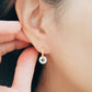 A woman adorns her ear with a small gold jade earring, complemented by white jade huggie hoops made from natural gemstones.