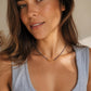 A close-up lifestyle shot of a woman with long brown hair wearing a delicate beaded Kyanite necklace with blue and gold beads, paired with a light blue-gray ribbed tank top.