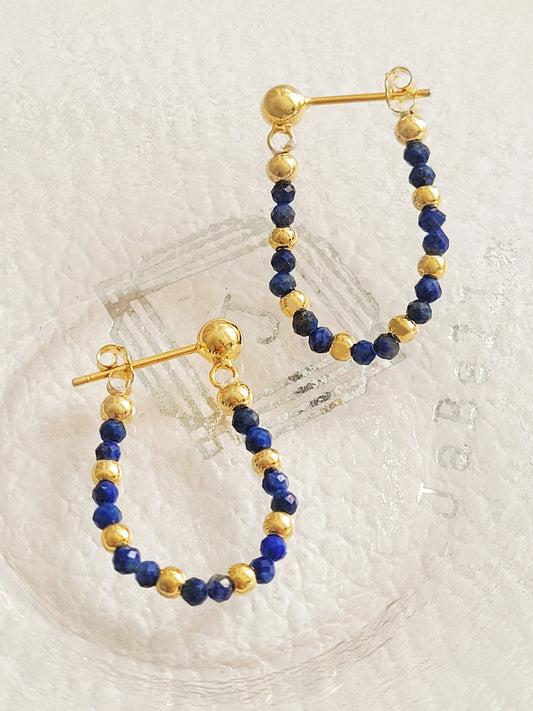 Hoop earrings with blue lapis lazuli gemstone and gold beads on a light background