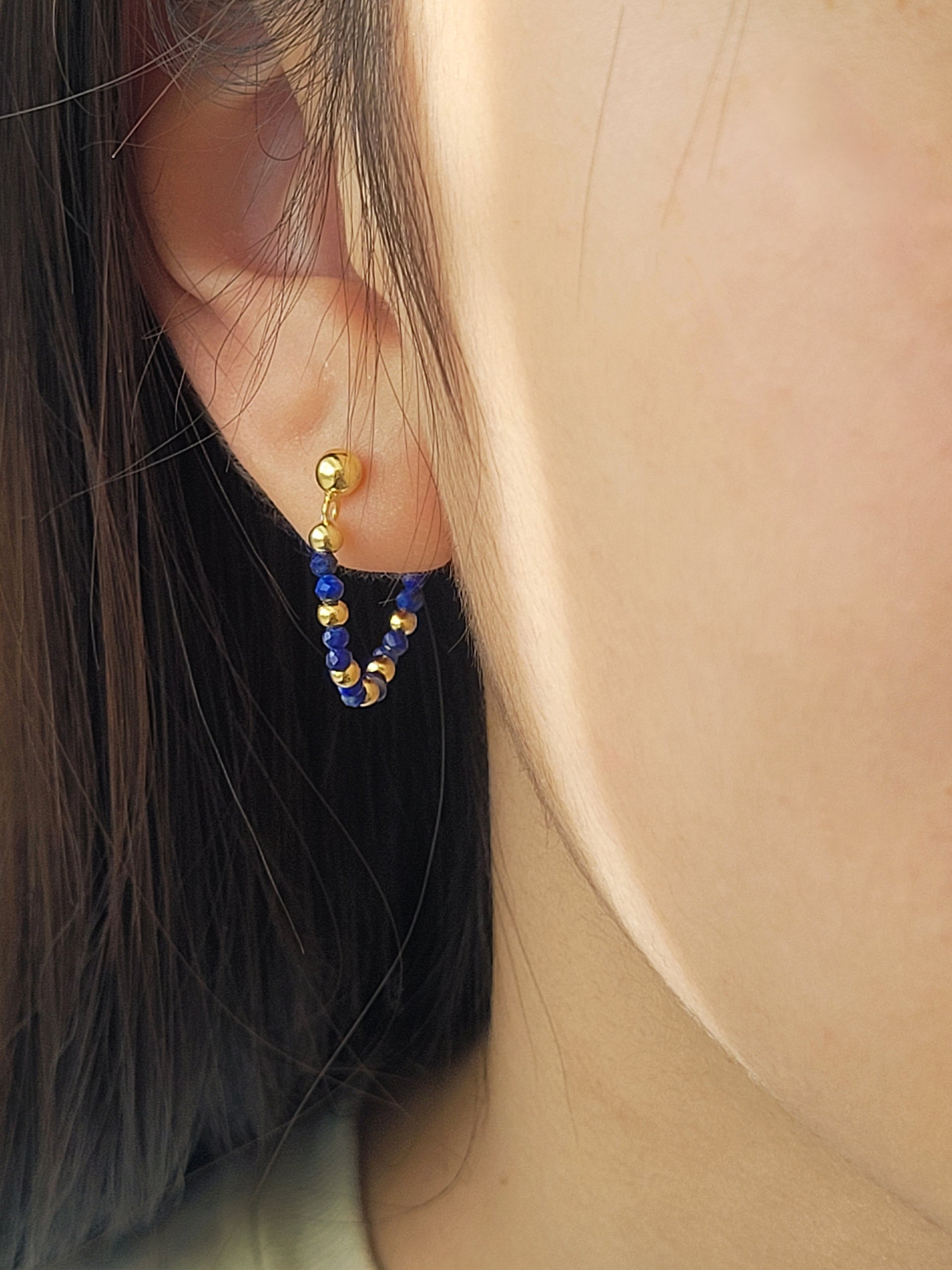 Close-up of an ear wearing a gold and blue gemstone beaded earring.