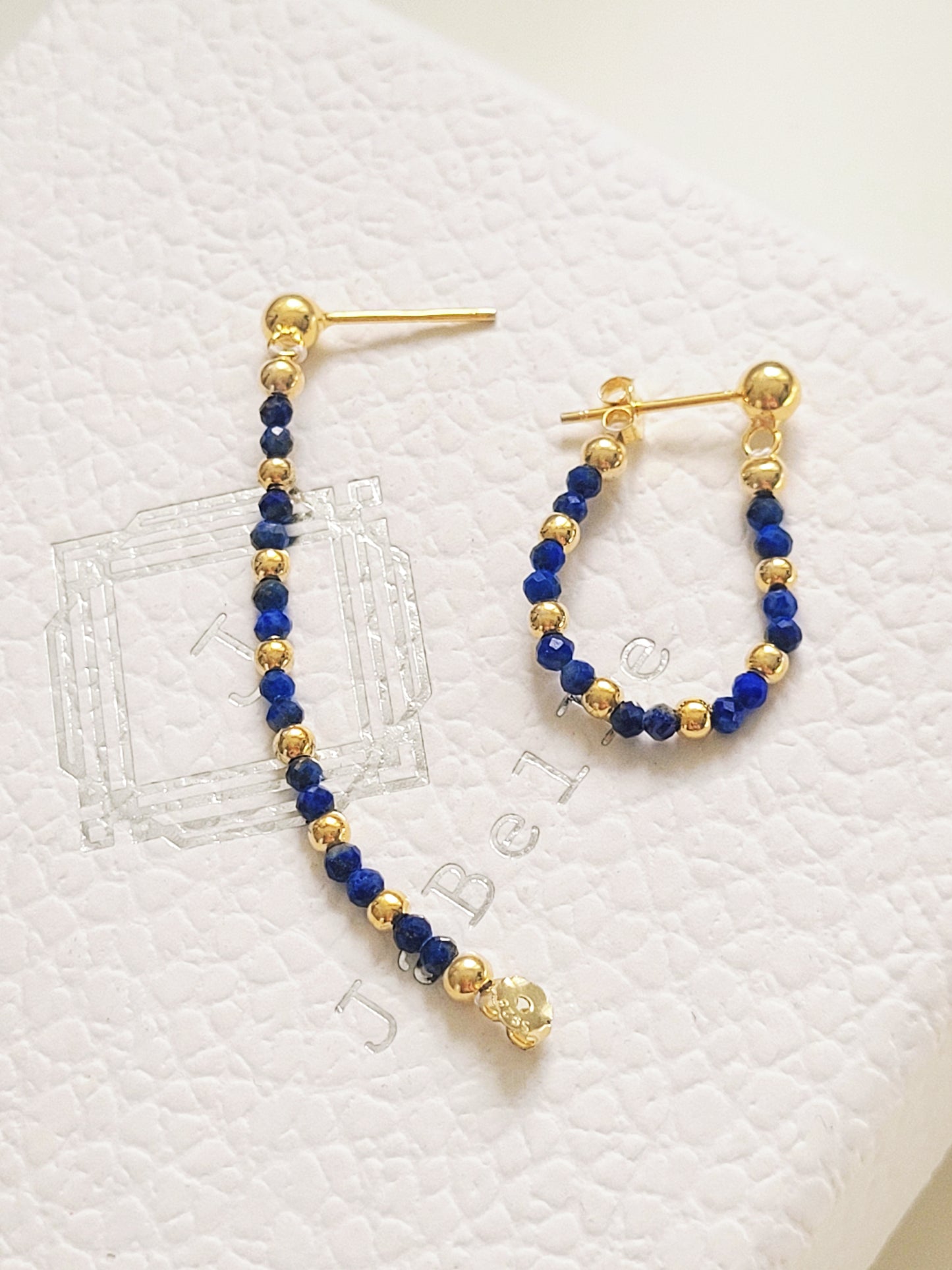 Pair of hoop earrings with blue beads and gold accents on a textured white surface.