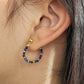 Close-up of an ear wearing a gold hoop earring with blue beads. Hamndmade jewellery gift for her