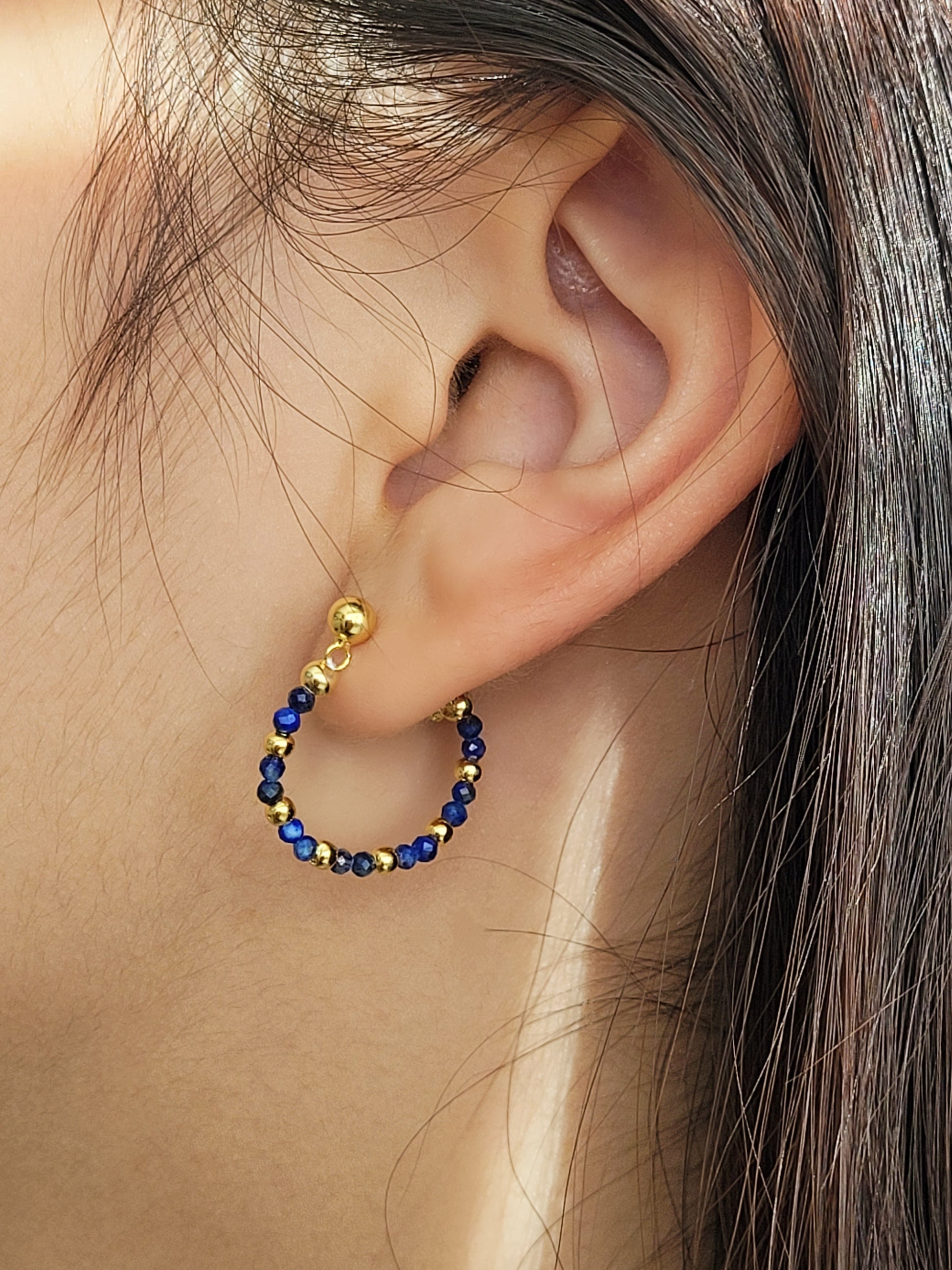 Close-up of an ear wearing a gold hoop earring with blue beads. Hamndmade jewellery gift for her