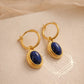 A pair of dainty gold hoop earrings with blue lapiz lazuli gemstone on a beige fabric background.