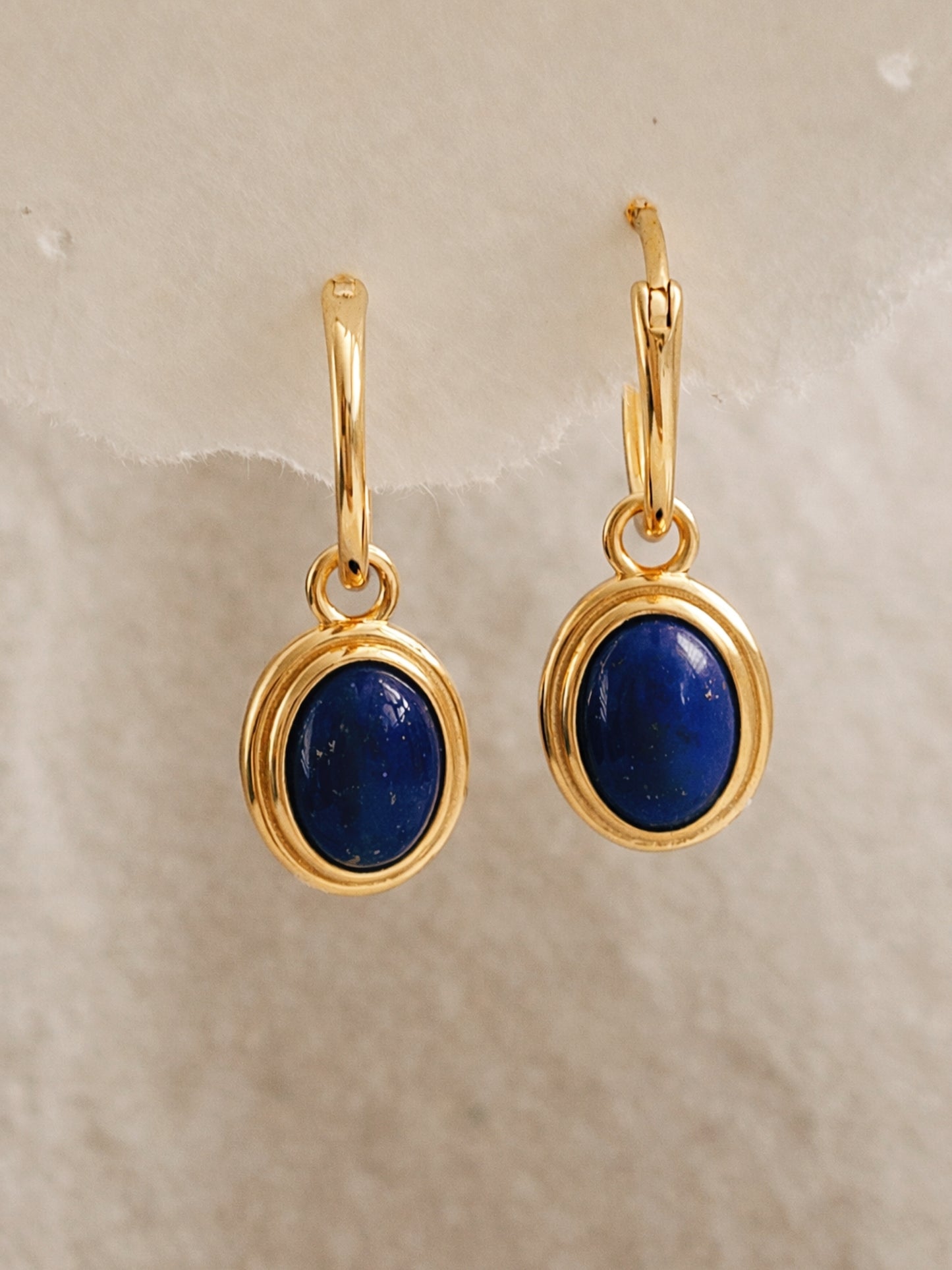 Gold earrings with blue stones on a beige background
