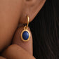Dainty gold earring with a blue lapis oval drop worn by a woman