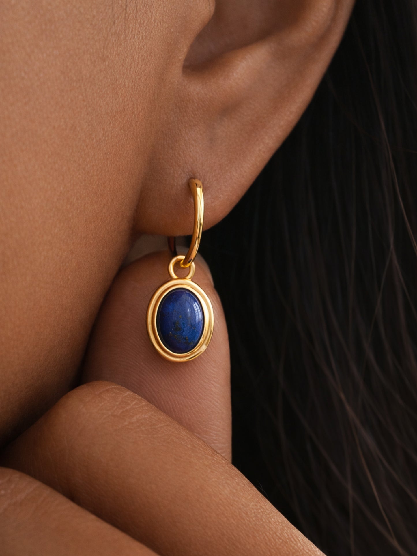 Dainty gold earring with a blue lapis oval drop worn by a woman