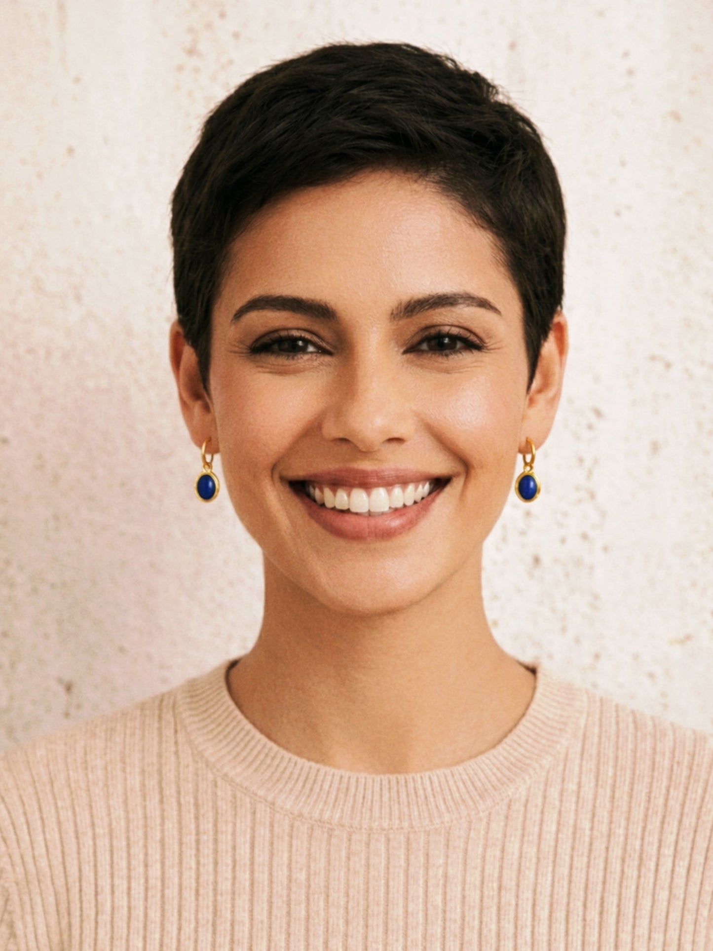 Woman with short black hair wearing minimalist lapis lazuli earrings against a neutral background.