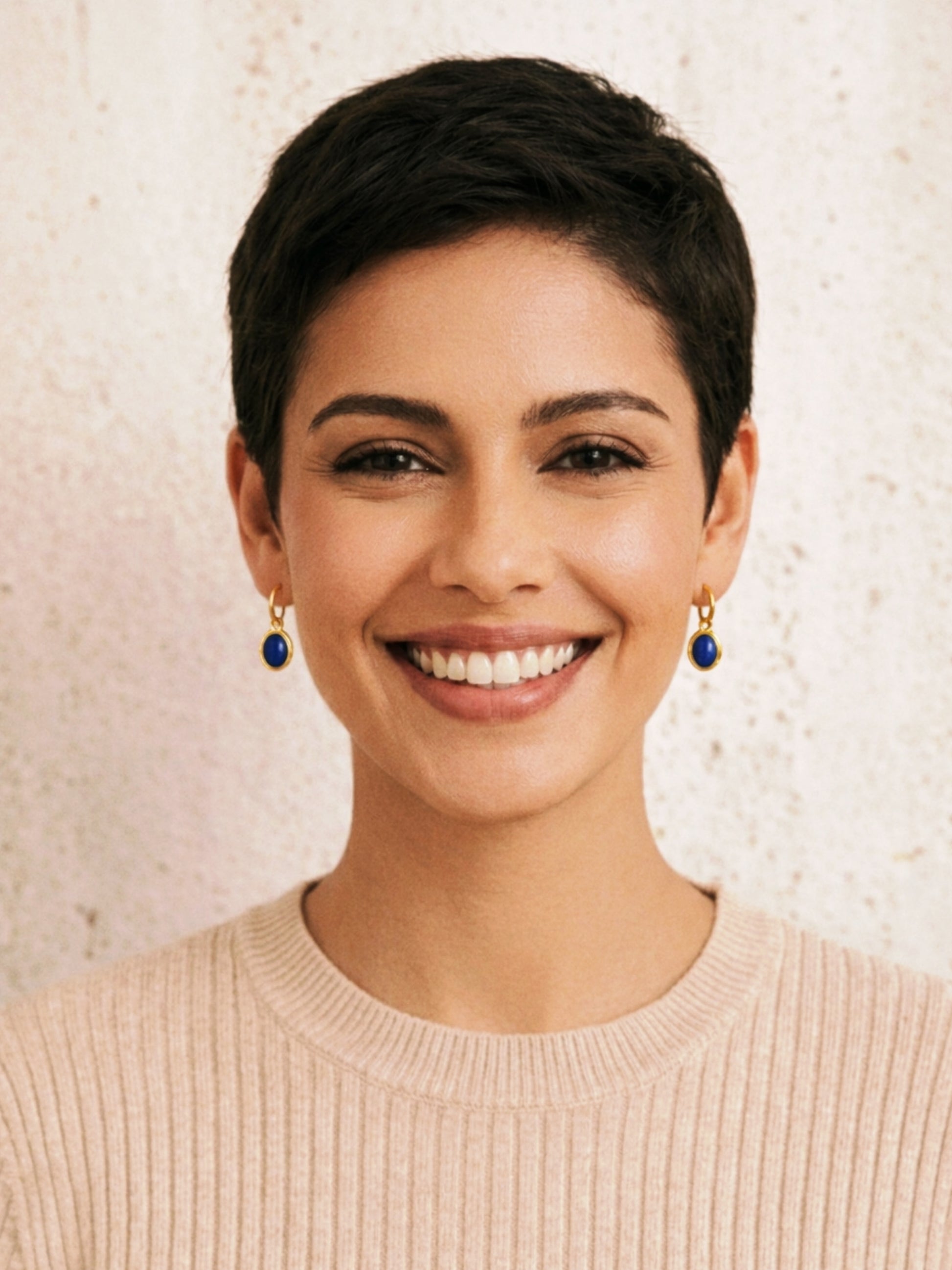 Woman with short black hair wearing minimalist lapis lazuli earrings against a neutral background.