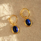 A pair of gold hoop earrings with blue lapis lazuli gemstone, the september birthstone, on a beige fabric.