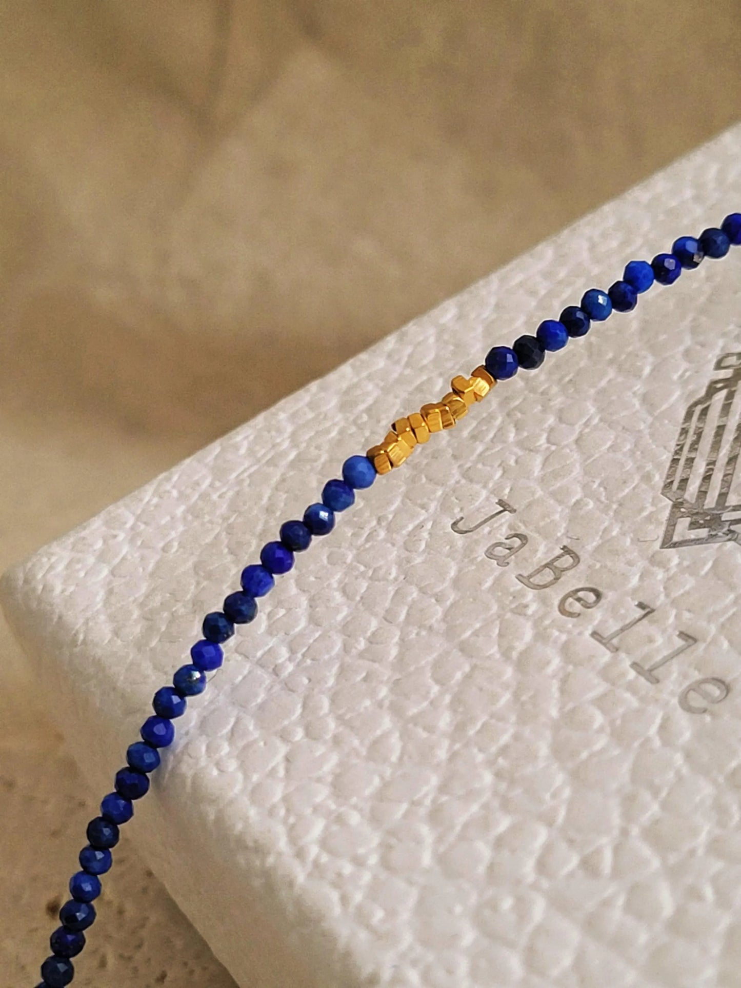Close up of a deep blue lapis lazuli gemstone and gold bead bracelet featuring faceted natural stone beads and gold-plated accents on JaBelle Jewellery box.