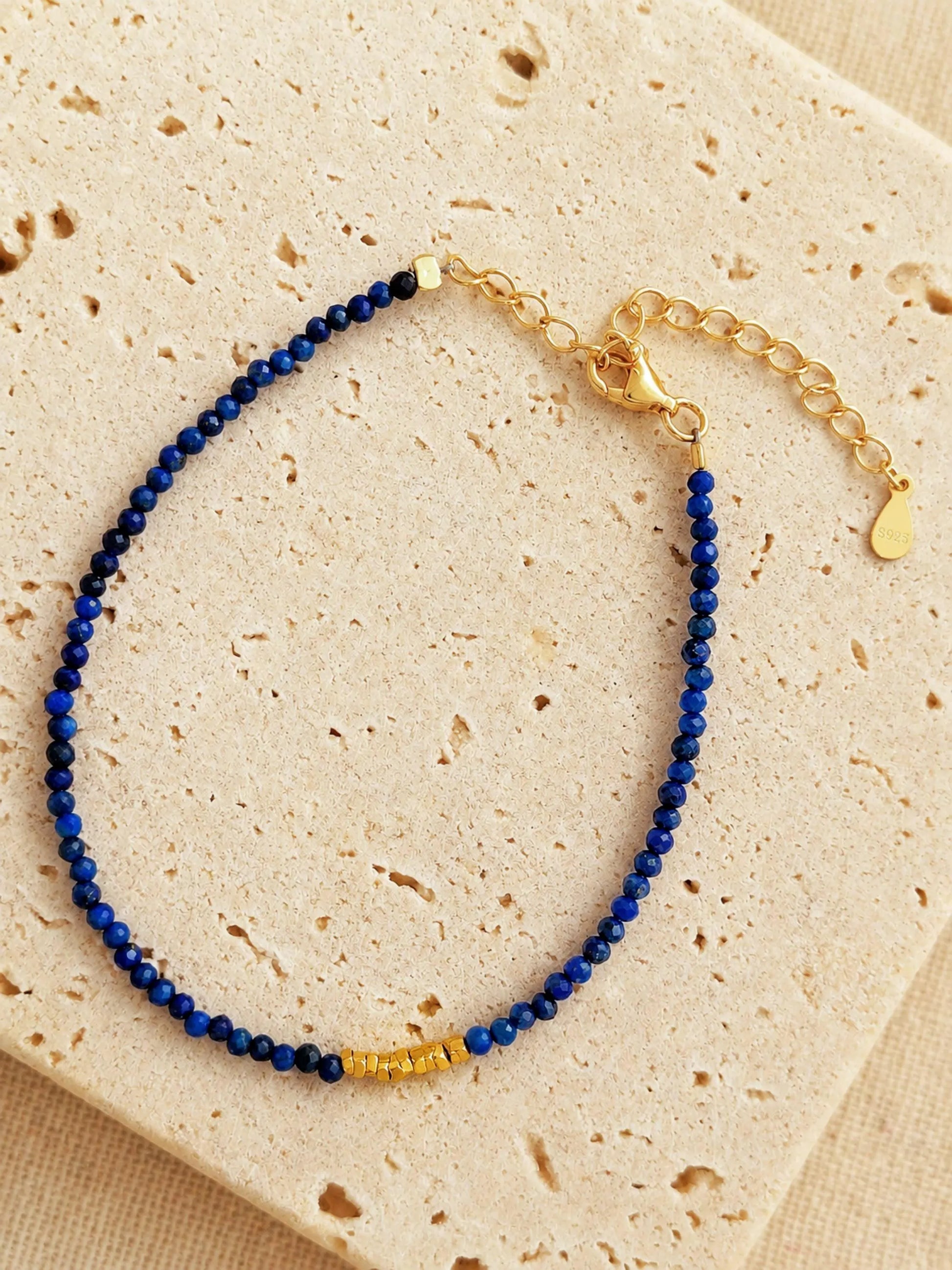 A beaded 18k gold vermeil bracelet featuring faceted lapis lazuli gemstone in deep blue color displayed on an aesthetic beige color stone, delicate and minimal style for everyday wear.