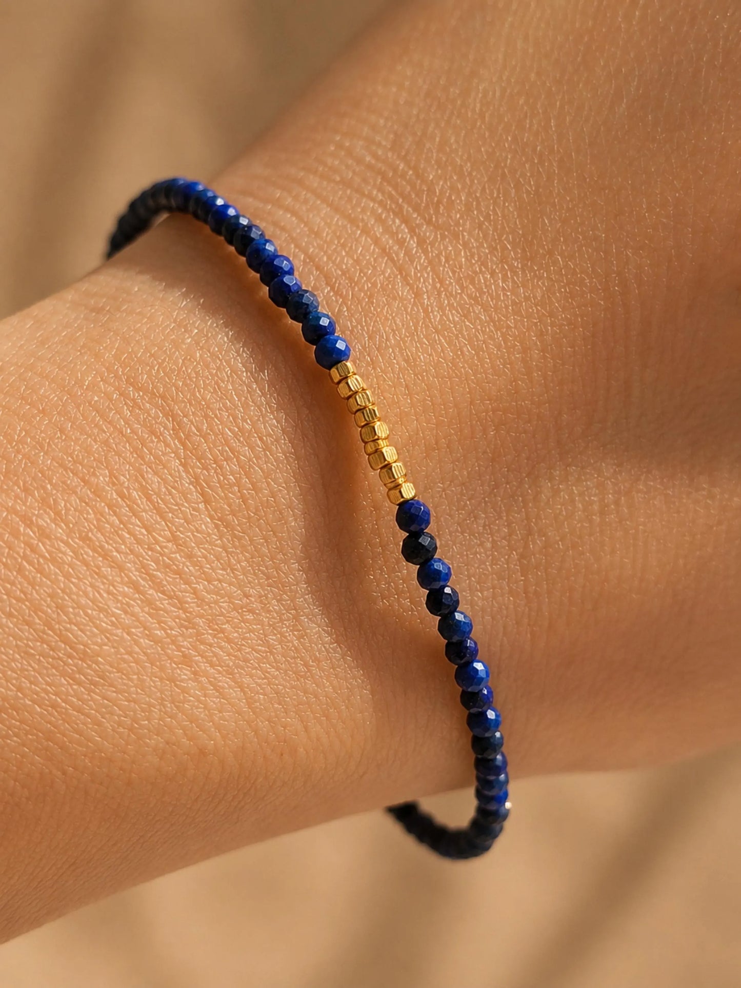 A delicate, handmade lapis lazuli bracelet, worn on woman wrist, featuring small faceted deep blue gemstone beads and gold vermeil accents, dainty minimalist jewellery