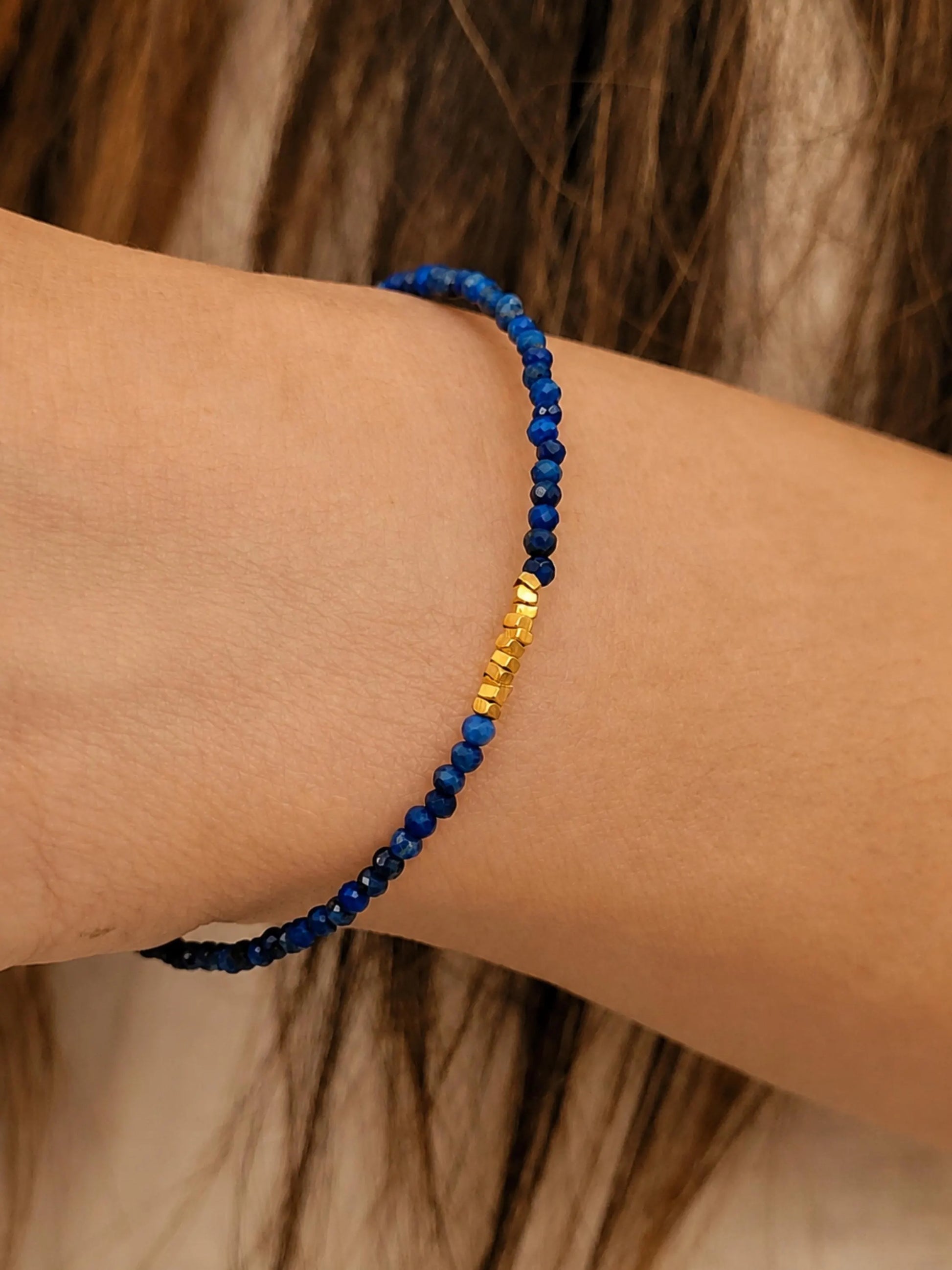 Model wearing a minimalist lapis lazuli beaded bracelet featuring tiny blue faceted gemstones and small gold accent beads.