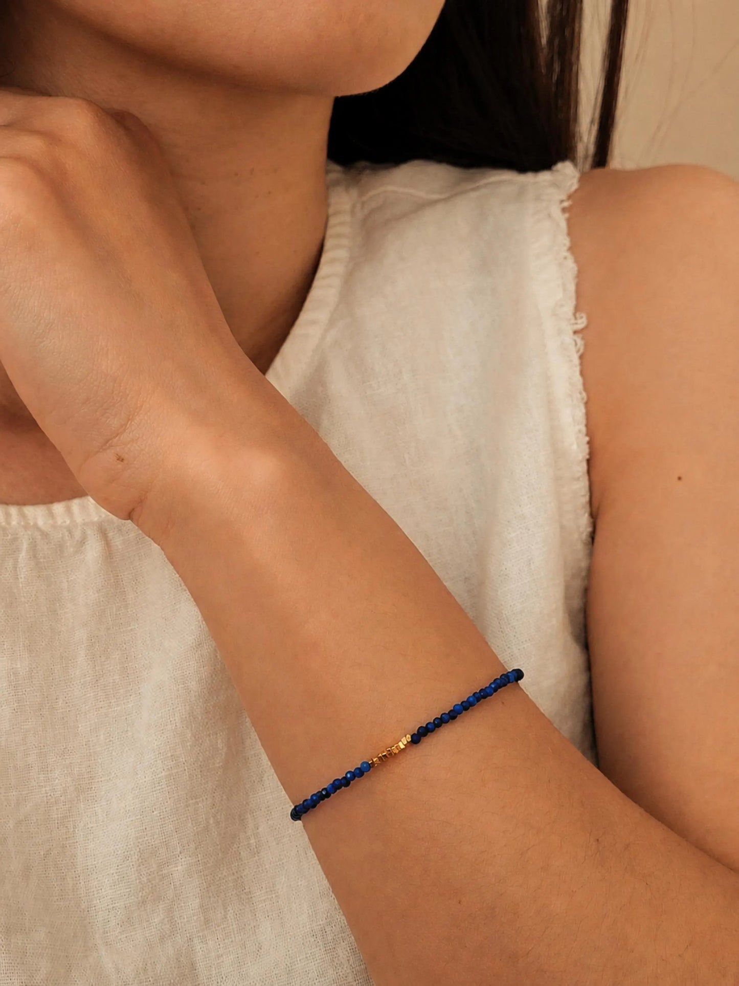 Model wearing white top in casual summer outfit with a delicate lapis lazuli beaded bracelet featuring tiny blue faceted gemstones and small gold accent beads.