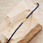A beaded 18kt gold vermeil bracelet featuring faceted lapis lazuli gemstone in deep blue color displayed on an aesthetic beige color stone, delicate and minimal style for everyday wear.