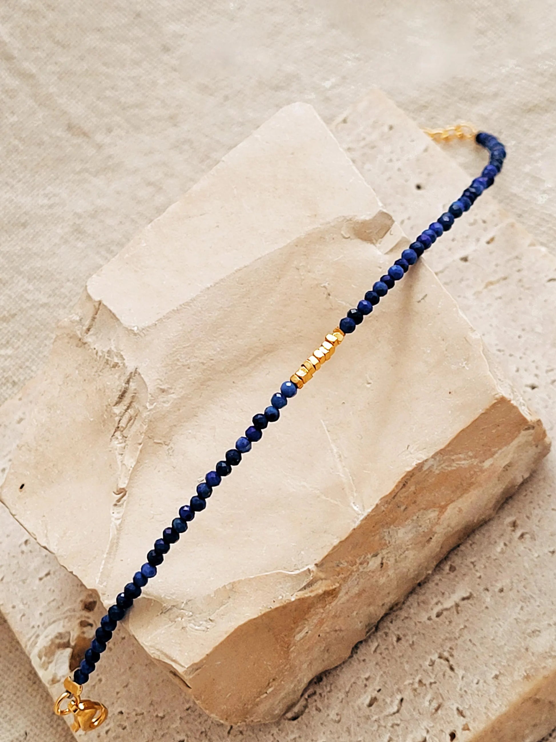 A beaded 18kt gold vermeil bracelet featuring faceted lapis lazuli gemstone in deep blue color displayed on an aesthetic beige color stone, delicate and minimal style for everyday wear.