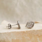 A pair of sculptural leaf cluster earrings displayed on a aesthetic beige stone surgace, showing the design in 925 sterling silver with pave cubic zirconia details.