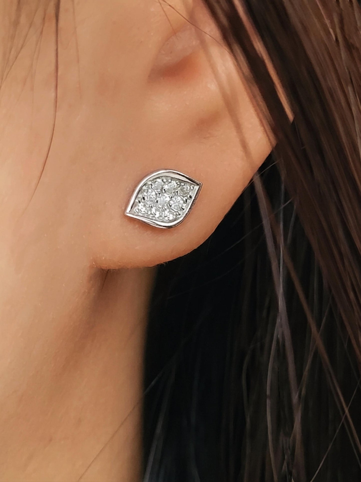 Close-up of a model wearing a dainty organic leaf-shaped stud earring in 925 sterling silver, featuring a cluster of shimmering pave CZ diamonds