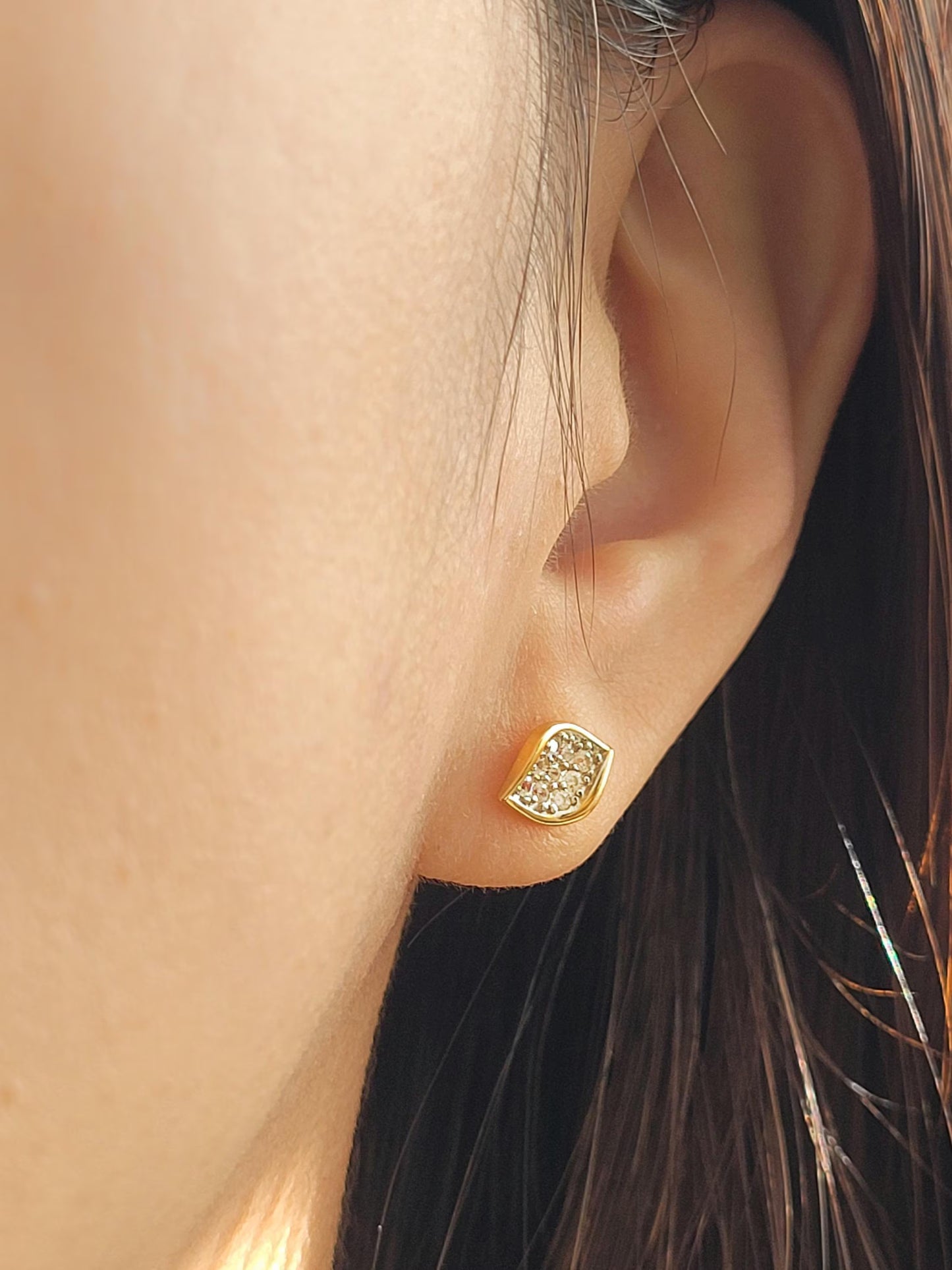 Close up of a woman wearing a gold stud earrings featuring natural leaf shape paved with cubic zirconia stone. 
