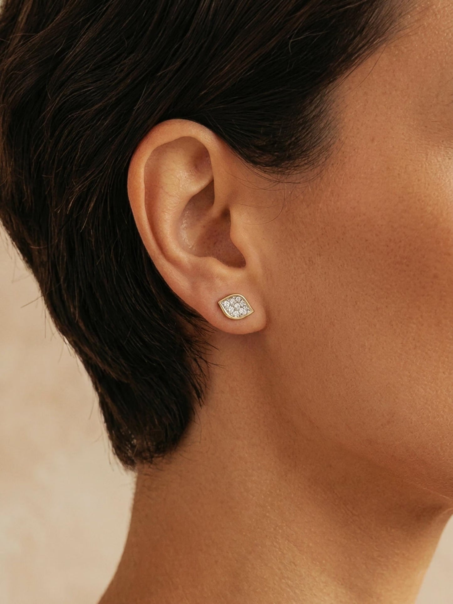 Close-up of a model wearing a dainty organic leaf-shaped stud earring in 18k gold vermeil, featuring a cluster of shimmering pave CZ diamonds against a neutral background.