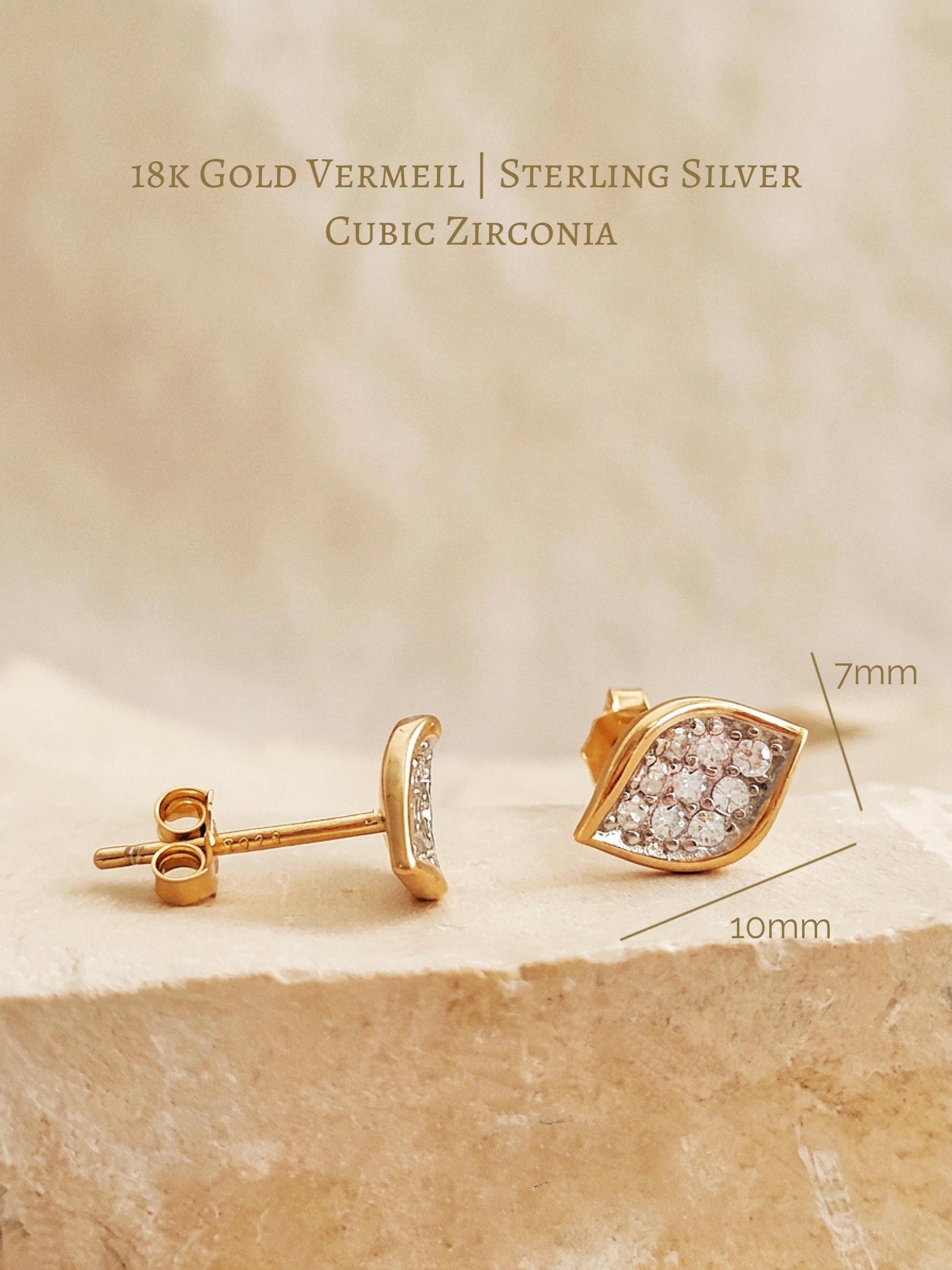 A sculptural leaf cluster earrings displayed on a aesthetic beige 
stone surface, showing the design in both 18k gold vermeil with pave cubic zirconia details.