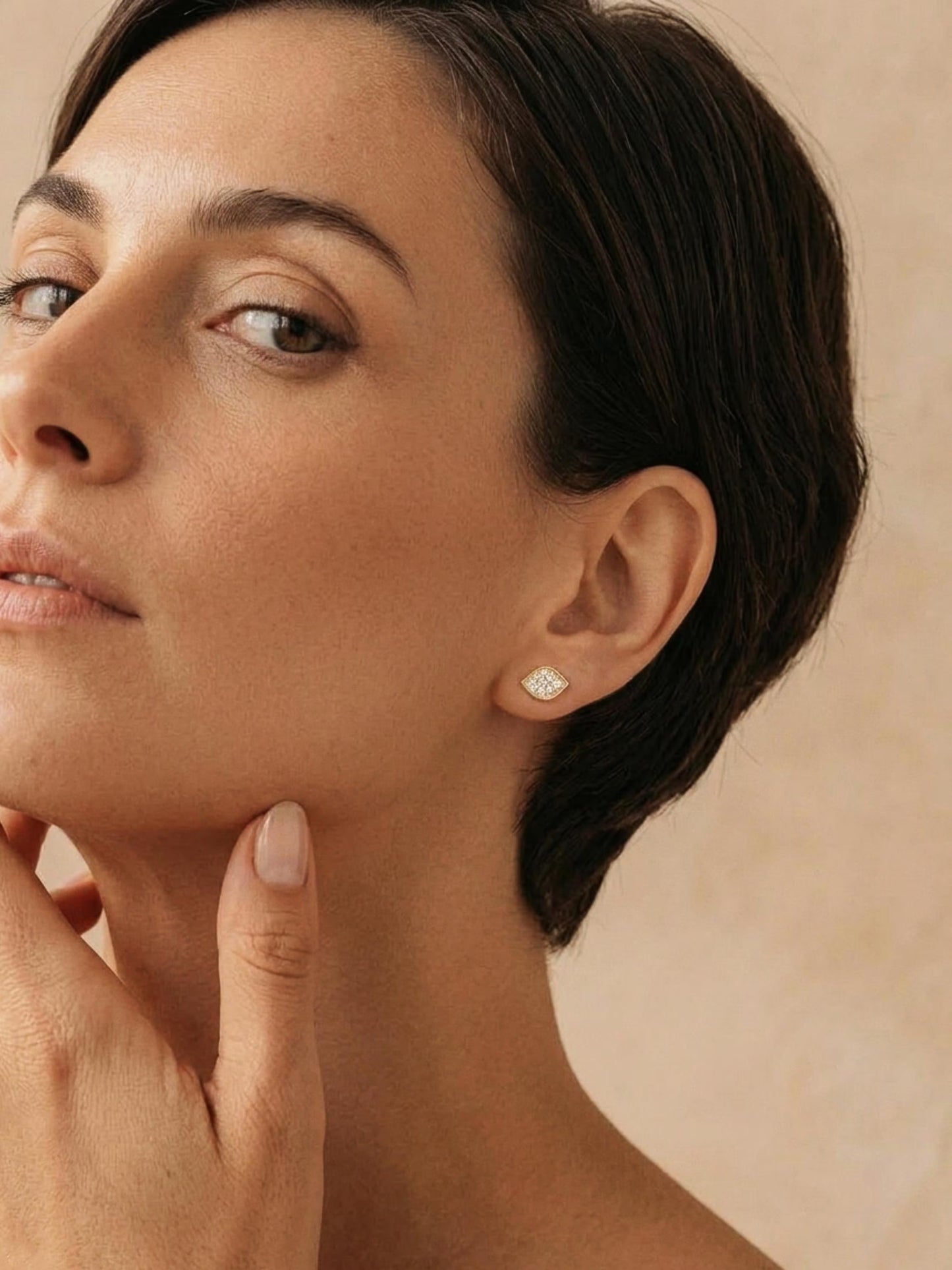A model wearing a dainty organic leaf-shaped stud earring in 18k gold vermeil, featuring a cluster of shimmering pave CZ diamonds against a neutral background. Minimalist dainty style jewellery designed in UK.
