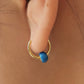 Close up of model ear wearing mini huggie earring with blue enamel bead, dainty and minimalist style