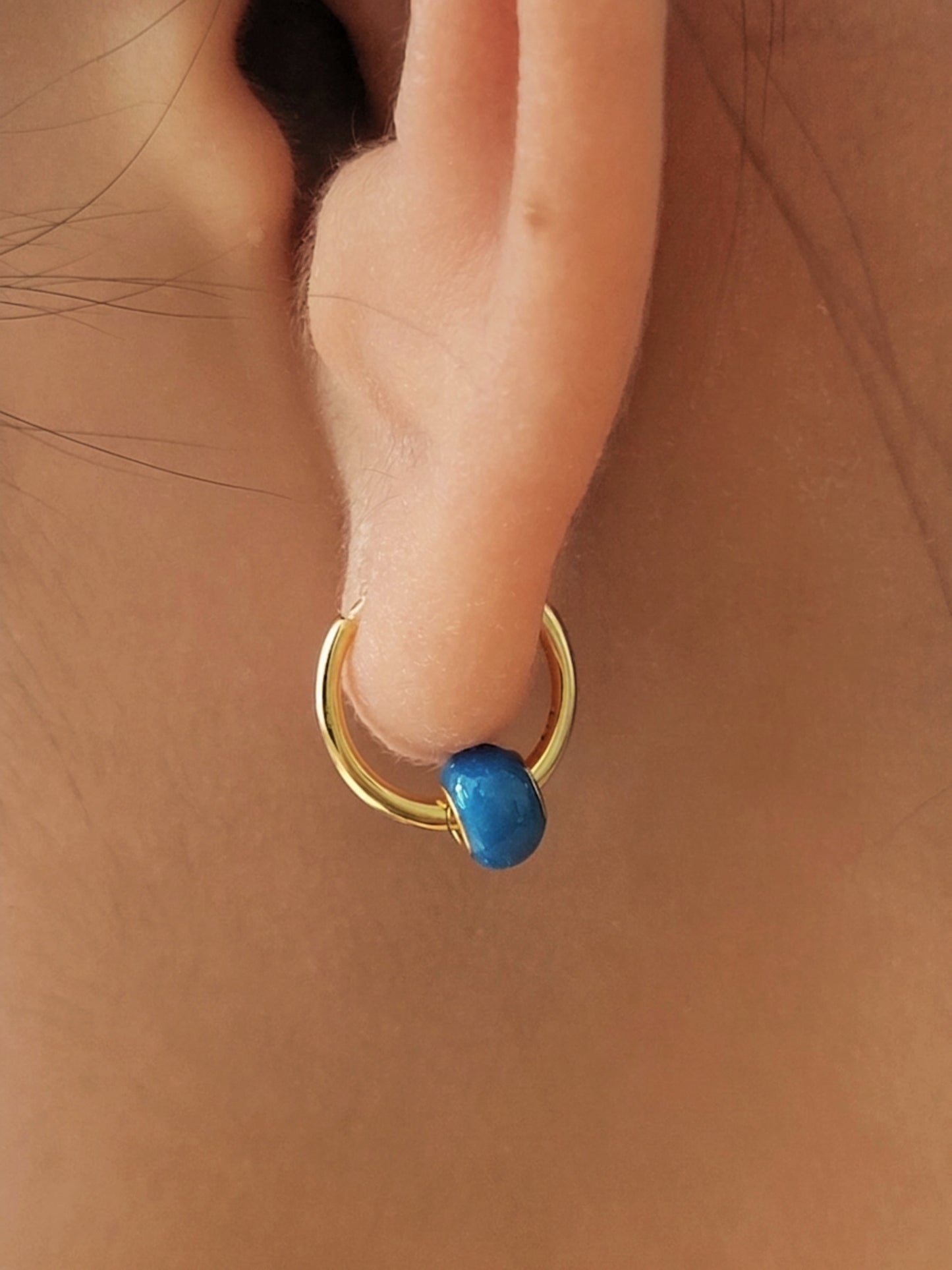 Close up of model ear wearing mini huggie earring with blue enamel bead, dainty and minimalist style