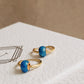 Side view of a pair of mini blue enamel bead huggie earrings on a JaBelle Jewellery box.