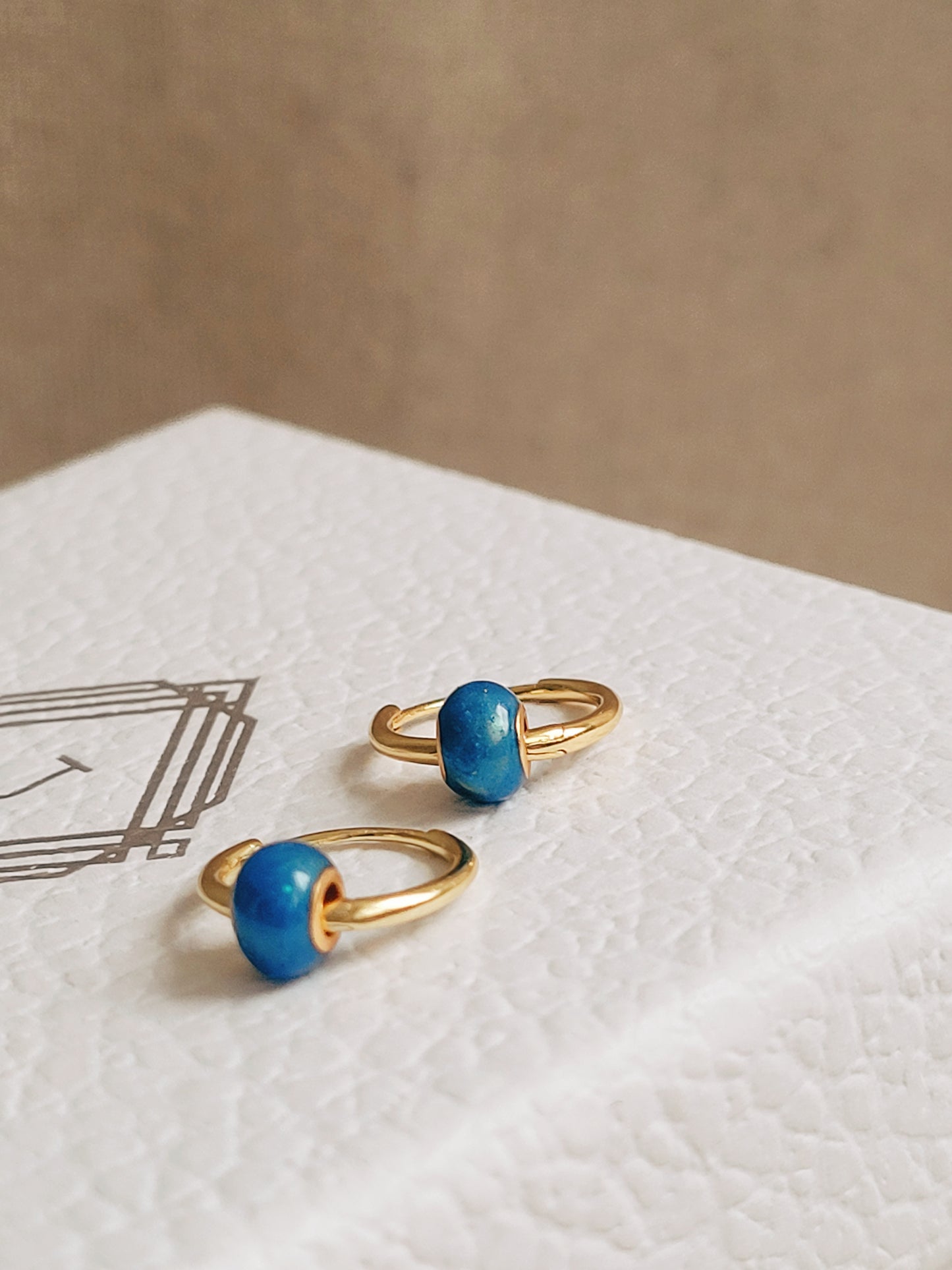 Side view of a pair of mini blue enamel bead huggie earrings on a JaBelle Jewellery box.