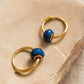 A pair of mini blue enamel bead huggie earrings displayed on an aesthetic beige color stone surface, showcasing its dainty and minimalist details.