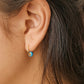 Close-up of an ear wearing a gold hoop earring with a blue enamel bead, crafted in London UK