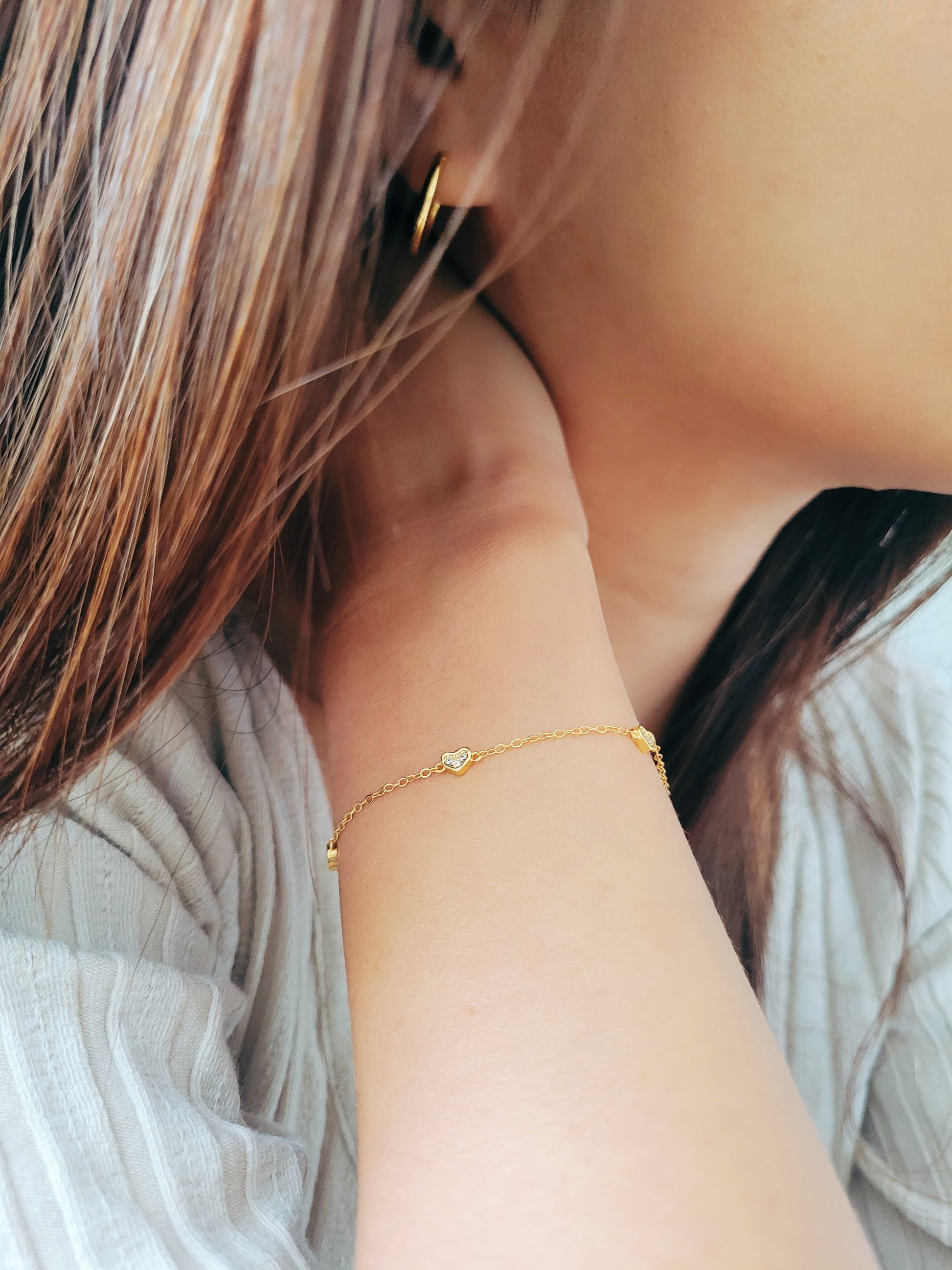 A woman wearing the mini heart bracelet everyday and mated with her gold hoop earrings.