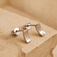 A pair of tiny silver stud earrings in curved bar shape on a beige stone surface, simple and minimal style.