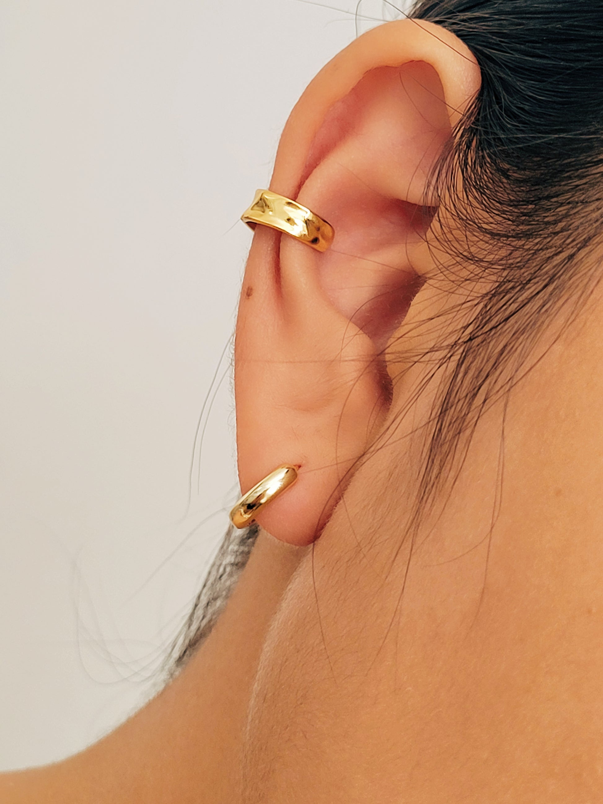 Close-up of a person wearing minimalist gold ear cuff earring against a neutral background