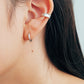 Close-up of an ear wearing a textured silver ear cuff earring paired with a simple hoop earrings with a neutral background