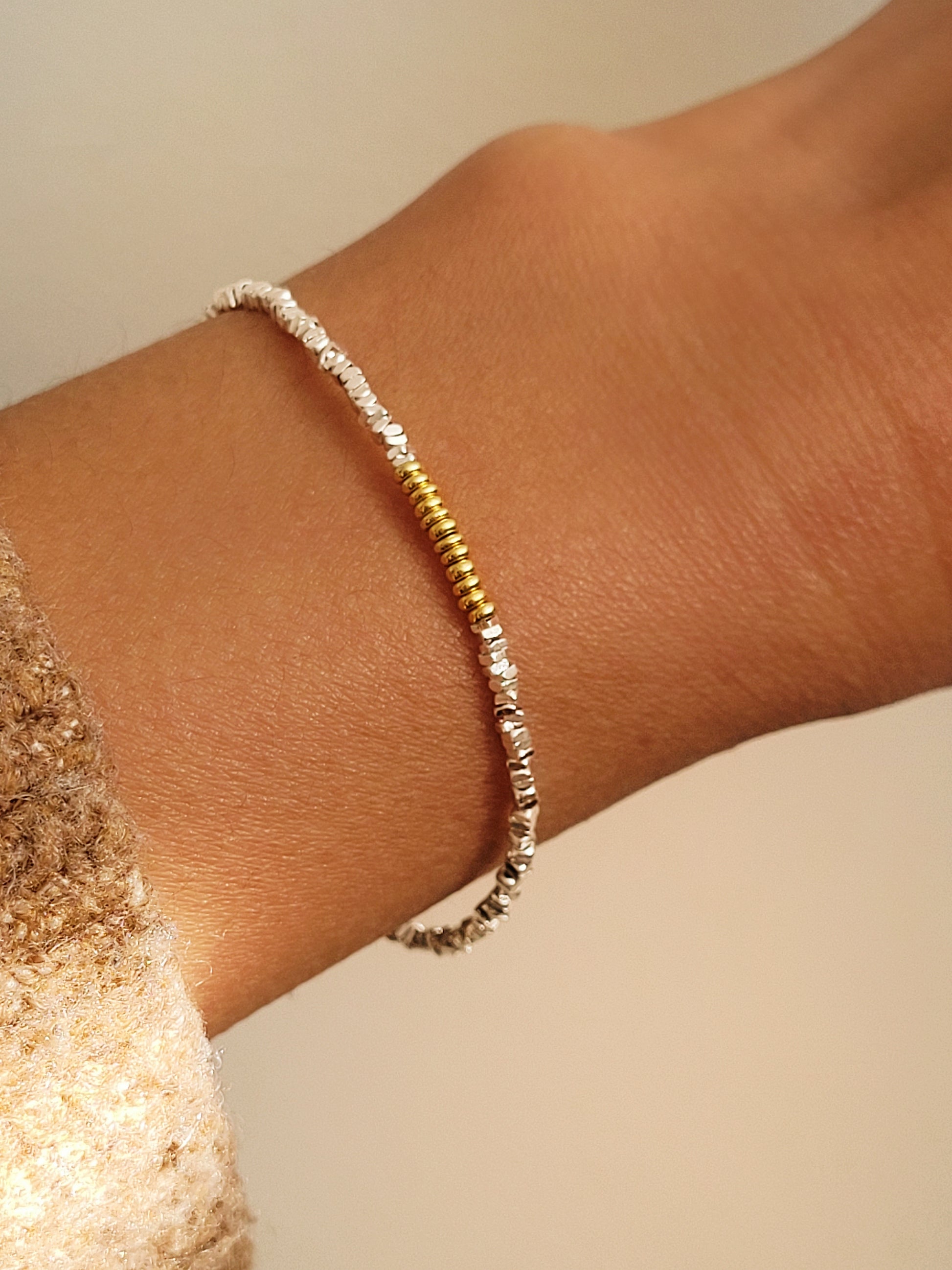 Close-up of a wrist wearing a mixed metal bracelet crafted in sterling silver and gold beads on a neutral background