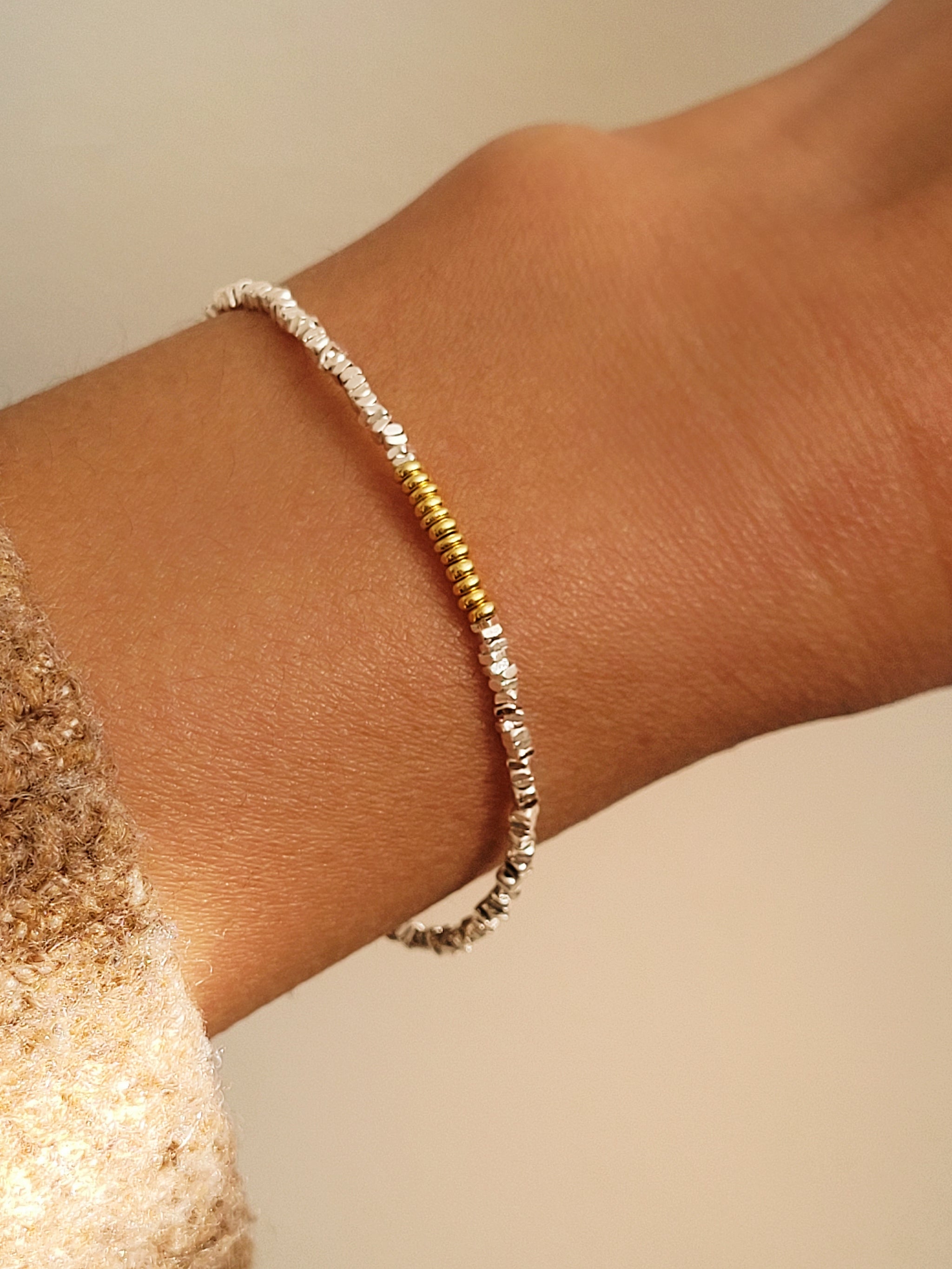 Close-up of a wrist wearing a mixed metal bracelet crafted in sterling silver and gold beads on a neutral background