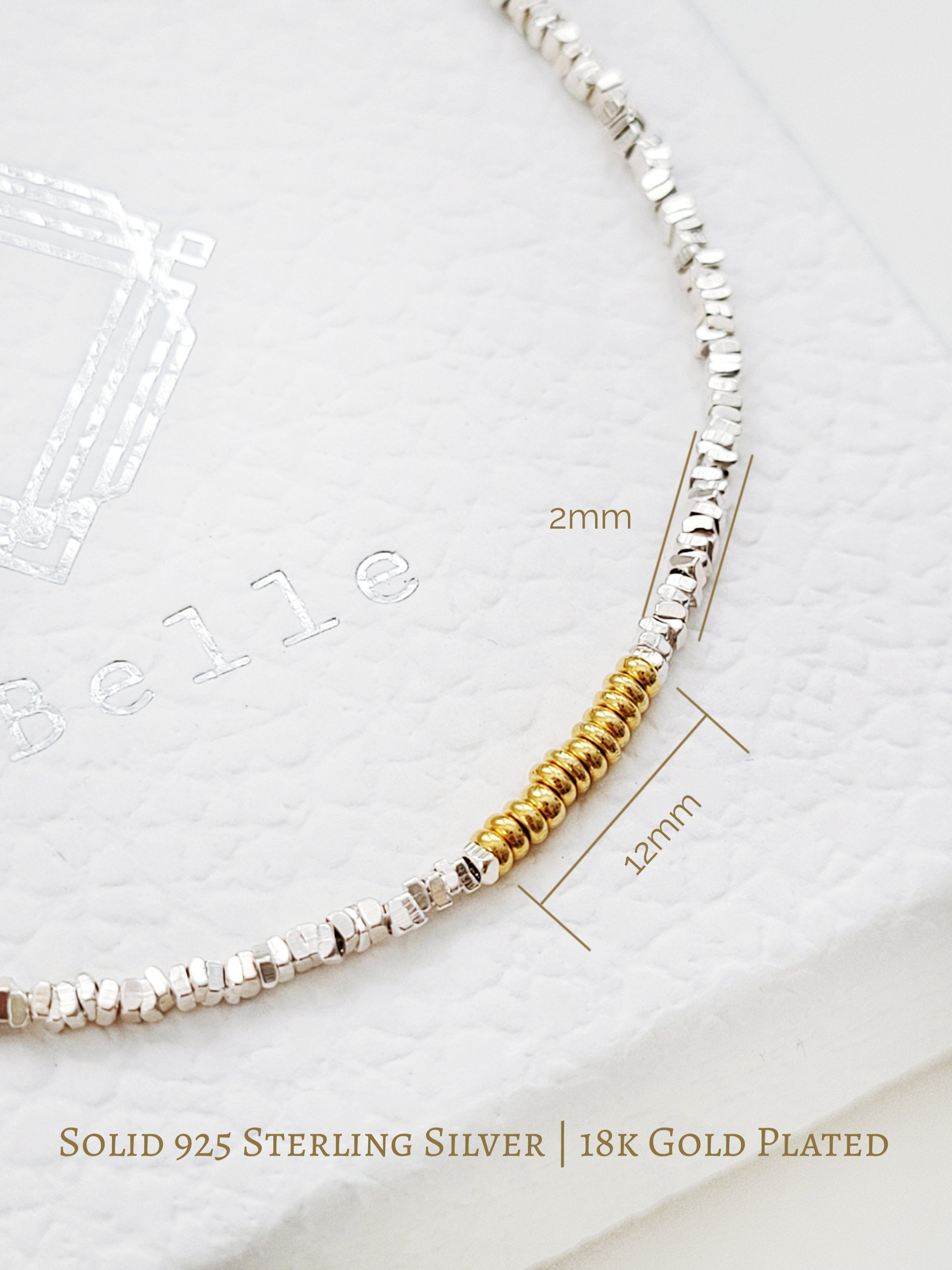 Close up of a sterling silver beaded bangle bracelet with 18k gold donut beads on a jewellery box.