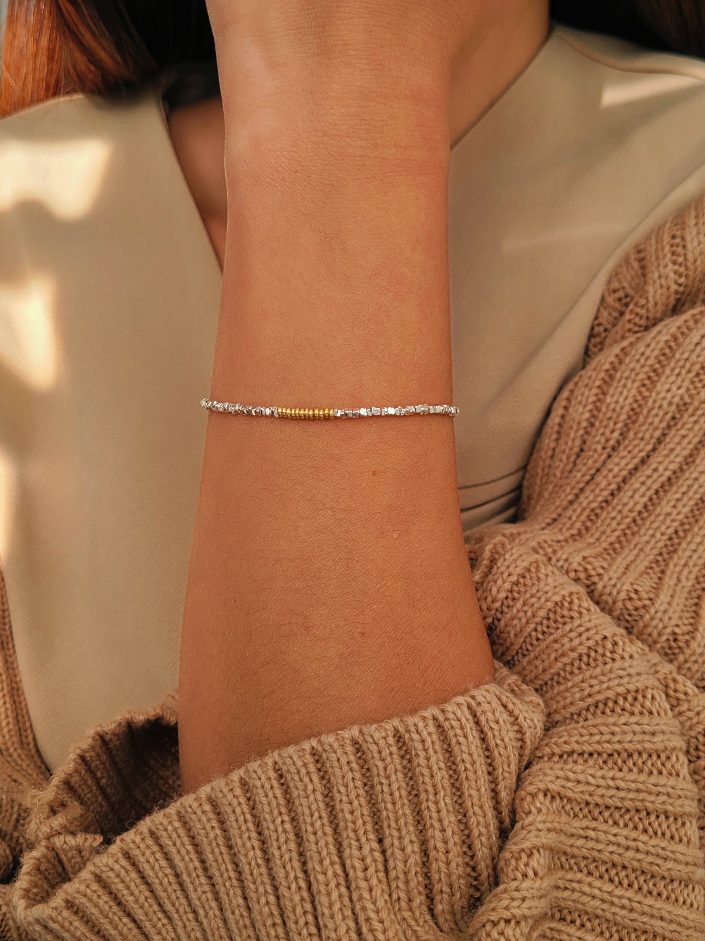 Close-up of a lady's wrist wearing a delicate mixed metal bracelet with a soft background.