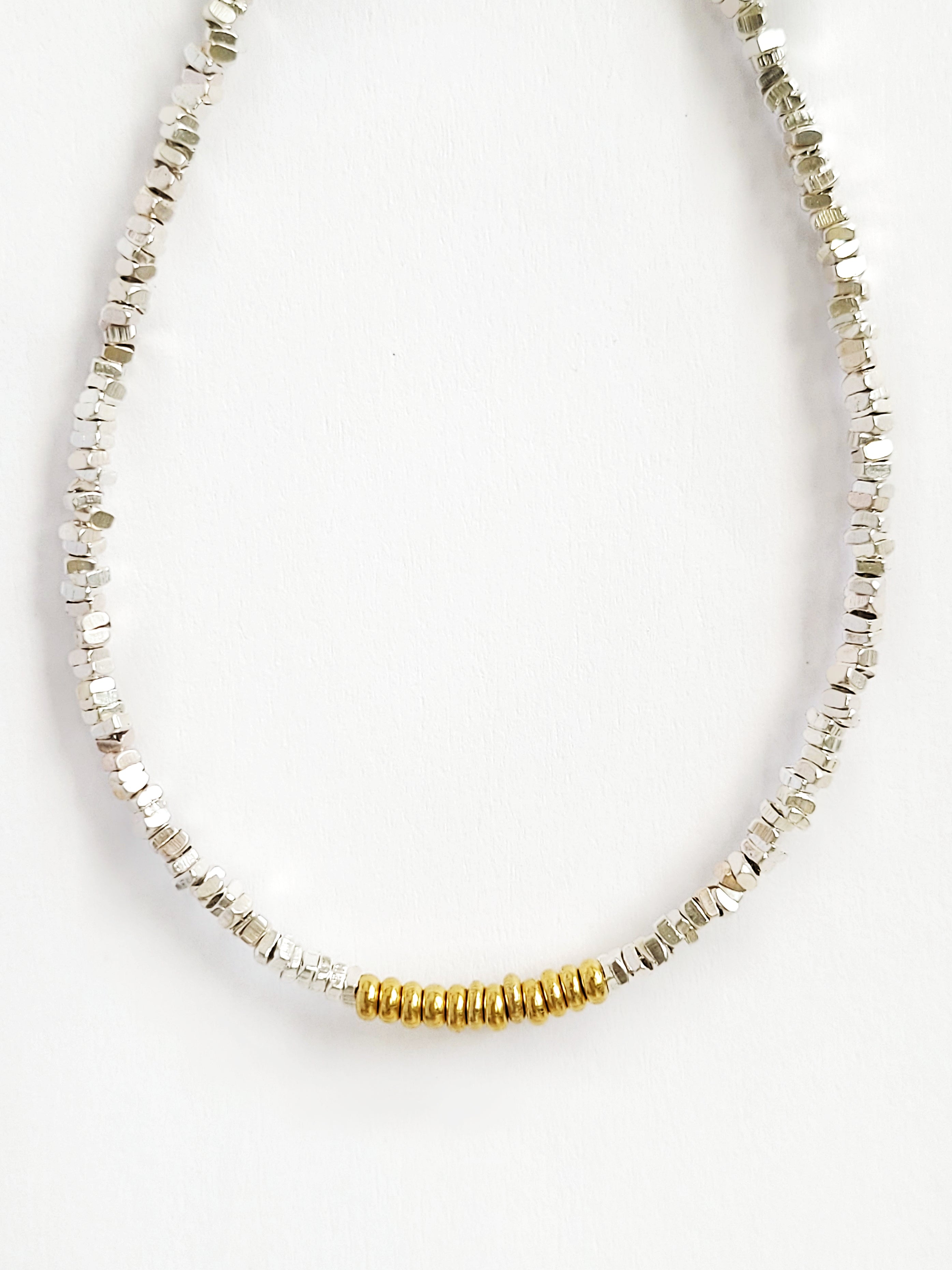A minimalist mixed metal bracelet with alternating gold and silver beads on a white background
