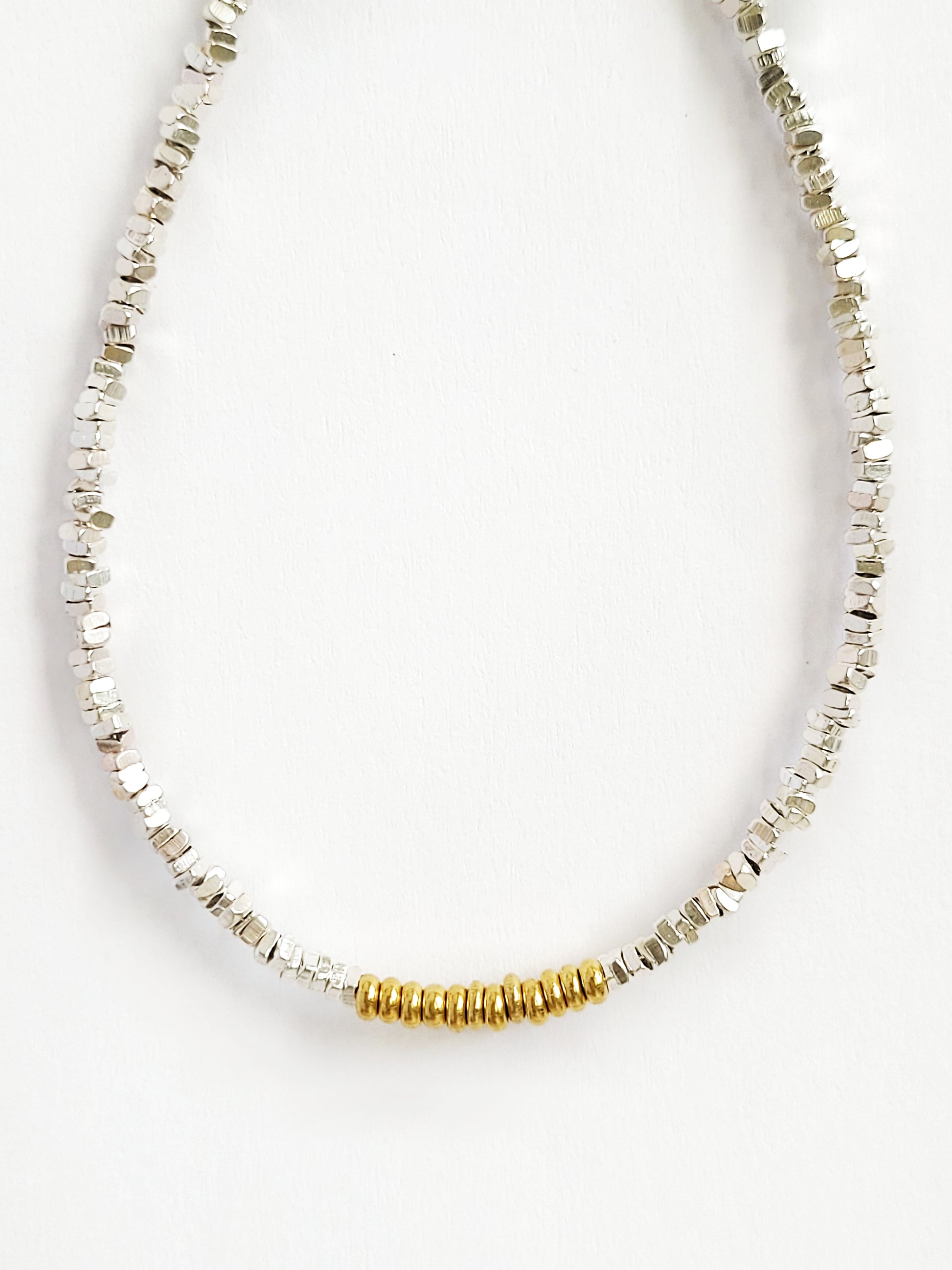 A minimalist mixed metal bracelet with alternating gold and silver beads on a white background