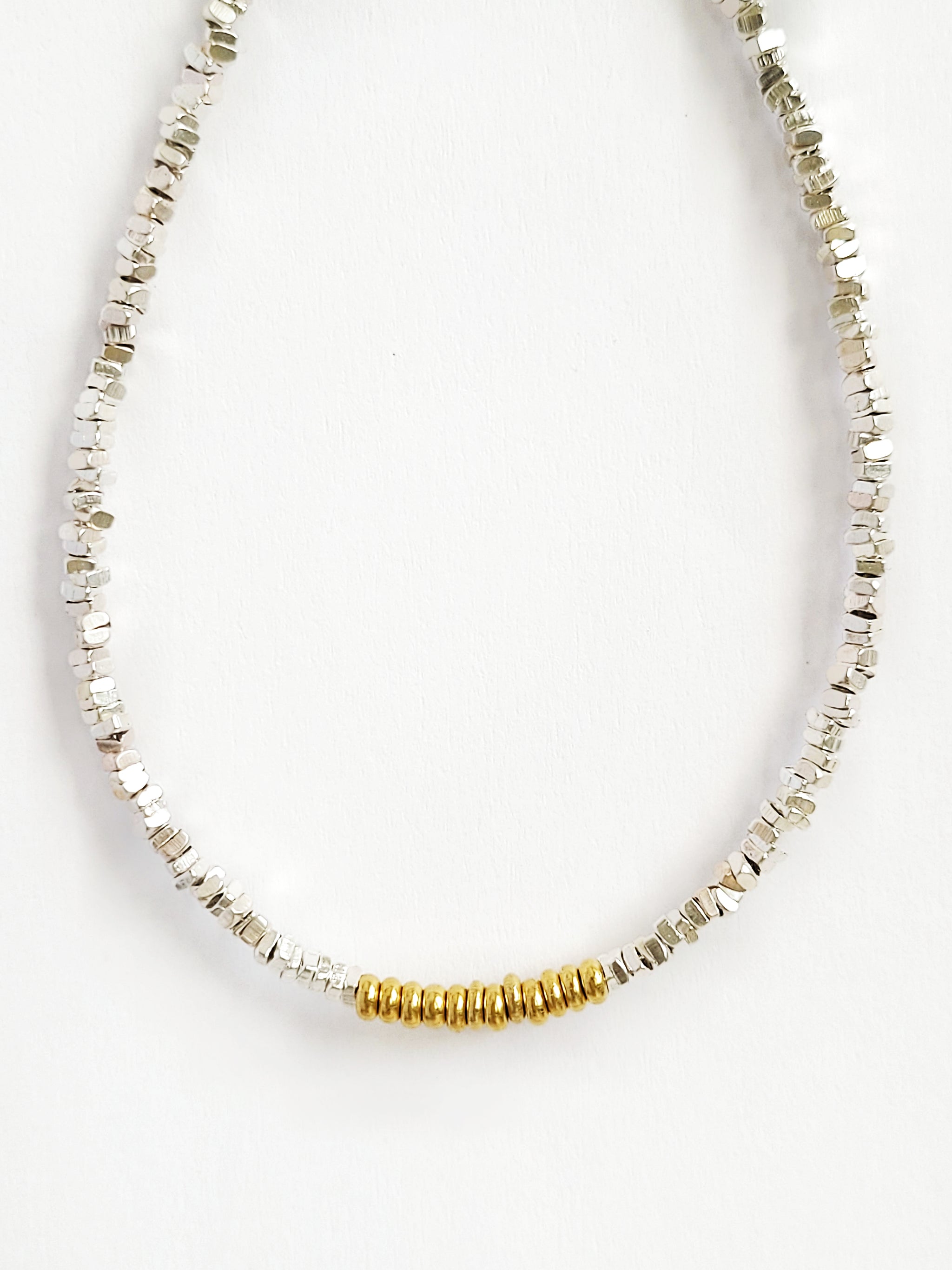 A minimalist mixed metal bracelet with alternating gold and silver beads on a white background