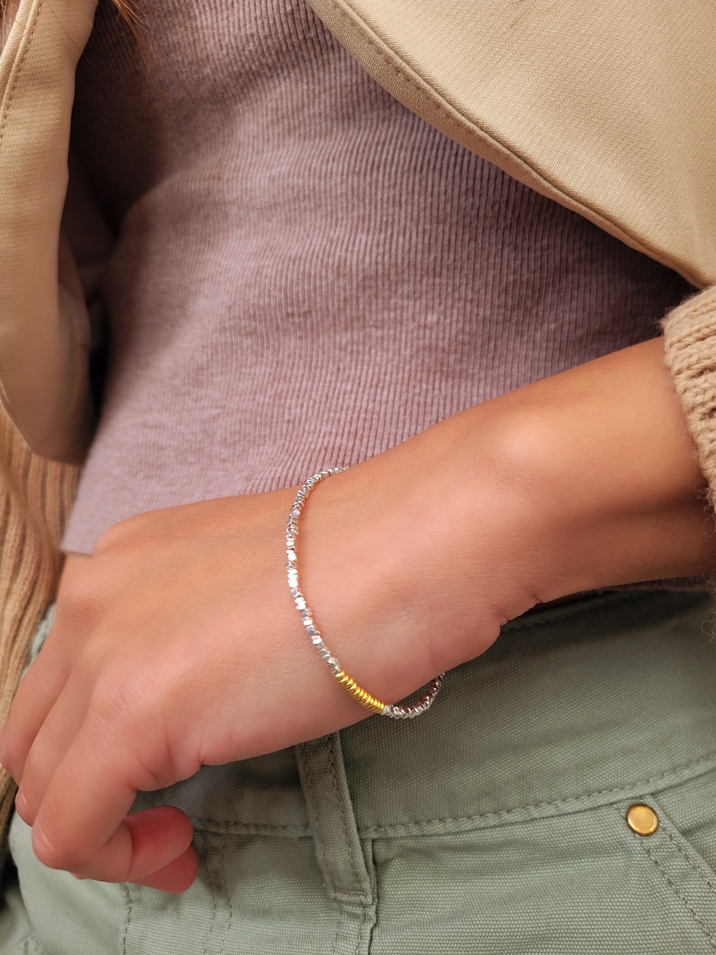 Close-up of a woman's wrist wearing a silver bangle bracelet with a beige jacket, showcasing its minimalist style