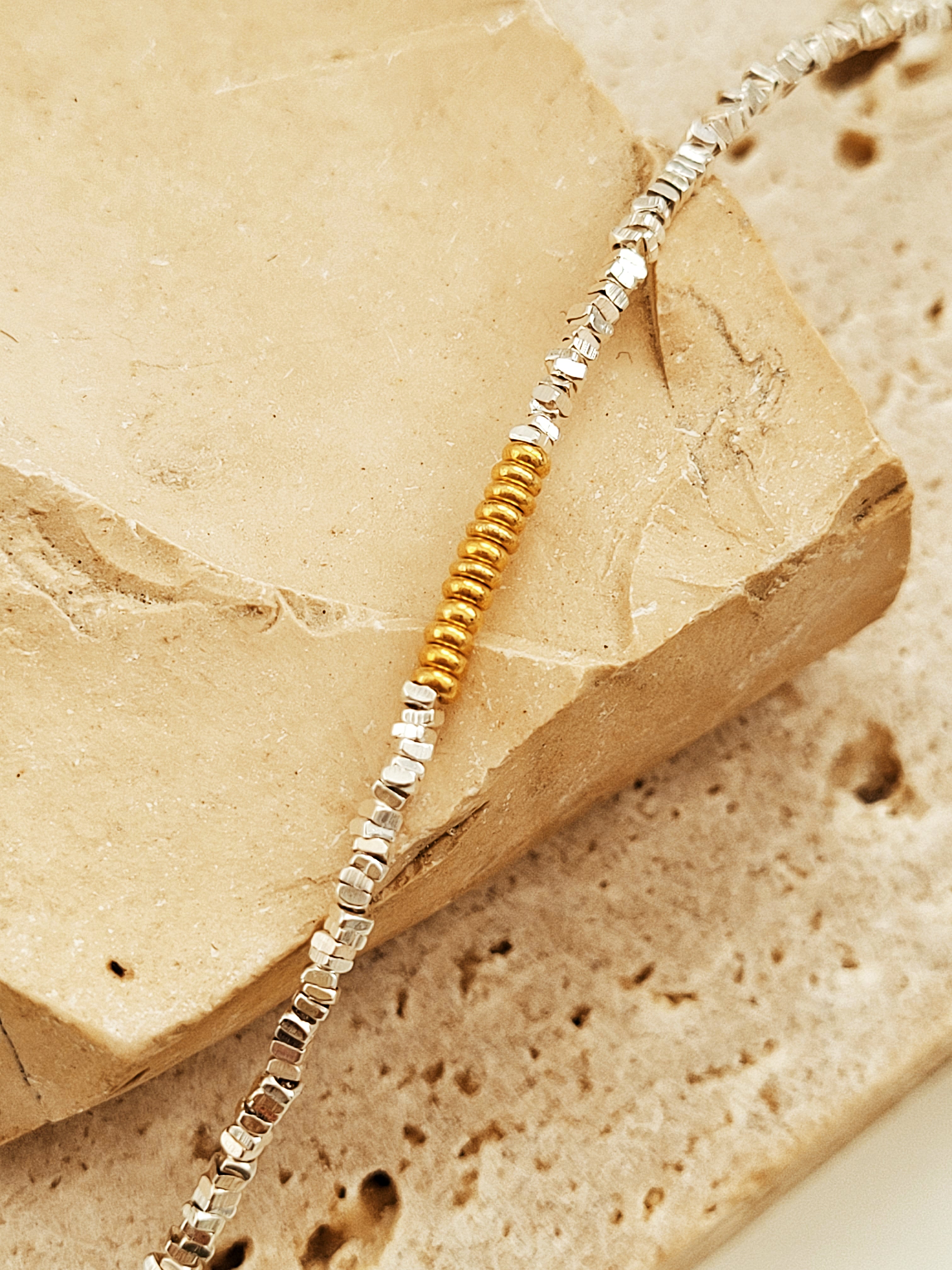 A sterling silver beaded bracelet with gold and silver beads on a stone surface