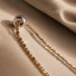 Close-up shot of a two-tone gold and silver beaded double chain necklace with a small silver ring charm resting on soft textured linen fabric.