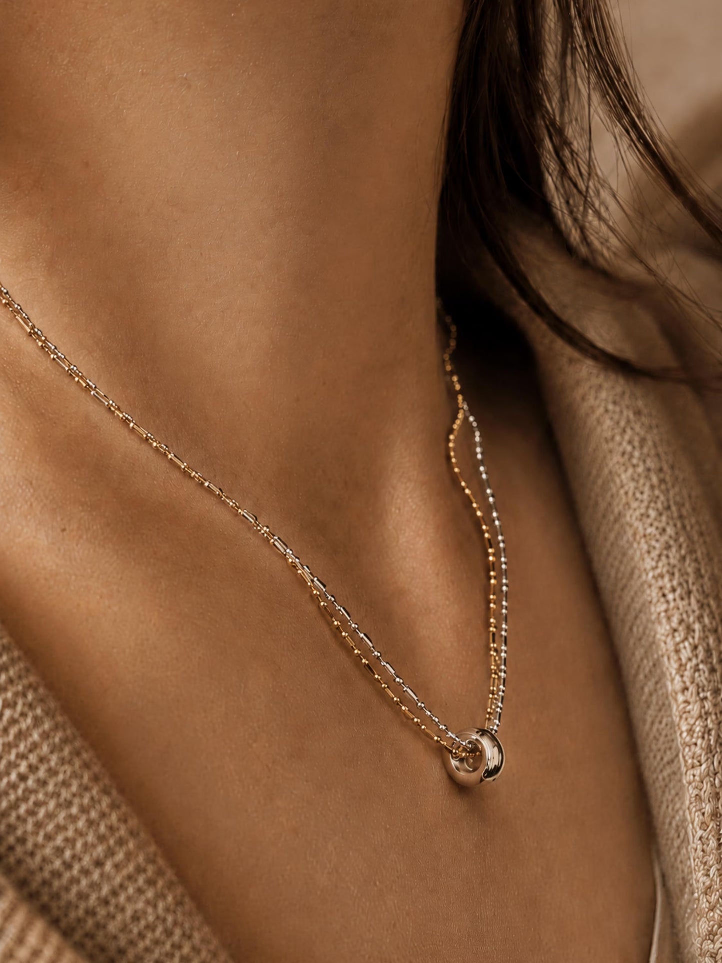 Woman wearing a dainty mixed metal double-chain necklace with a small round ring charm on her collarbone. Crafted in 18k gold plated sterling silver, minimalist and modern style jewellery.